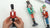 Hands holding a red-coated clay nutcracker soldier beside a green-coated drummer and a crowned nutcracker king.