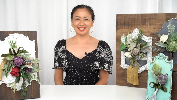 Instructor displaying decorative sculpted frames with clay artichokes, roses, foliage, ribbons, and tassels.