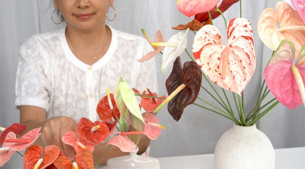 Instructor demonstrating handcrafted clay anthurium flowers in pink, red, cream, and burgundy, with a finished arrangement in a white vase.