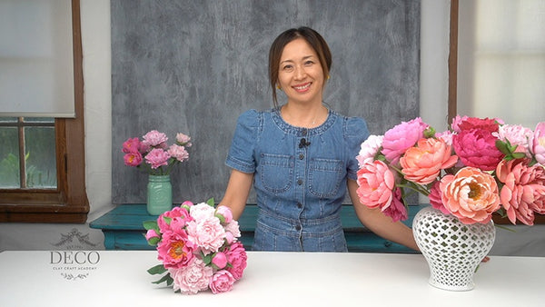 Instructor behind a pink clay peony bouquet and a white lattice vase filled with pink and peach peonies.