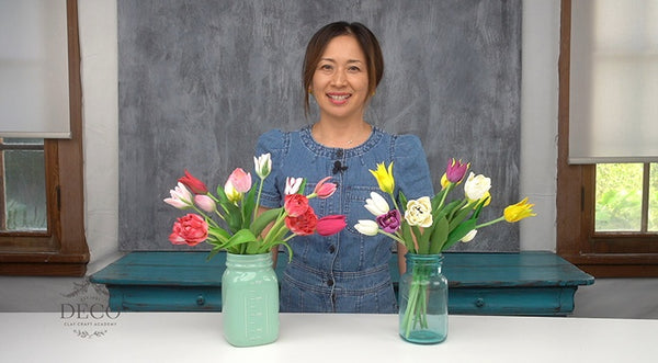 Instructor standing behind two glass vases filled with colorful handcrafted clay tulips and green leaves.⠋