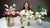Instructor behind a display of white and pale pink clay calla lily bouquets and mixed floral arrangements in glass vases.