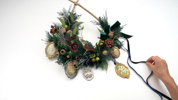 Christmas swag with dark red cosmos flowers, eucalyptus nuts and leaves, evergreen foliage, antique-style frame ornaments, and a dark green ribbon.⠋
