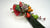 Japanese New Year arrangement with ornamental clay kale, orange fruits, red and green gourds, a red fan, plum blossoms, and long pine foliage.