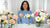 Instructor displaying handcrafted clay Hybrid Tea Roses and Rosa Rugosa flowers in pink, peach, cream, and yellow, arranged in glass vases.