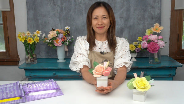 Instructor holding a small white box decorated with a peach clay rose, green leaves, and a pink macaron.