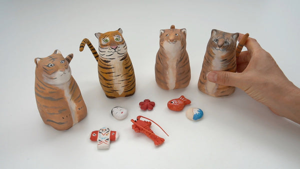 Four handcrafted clay tiger figures with orange and brown stripes, displayed with small colorful Japanese New Year ornaments.⠋