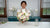 Instructor standing between a clay wedding bouquet of white orchids and pink flowers and white phalaenopsis orchid stems in a pale blue vase.